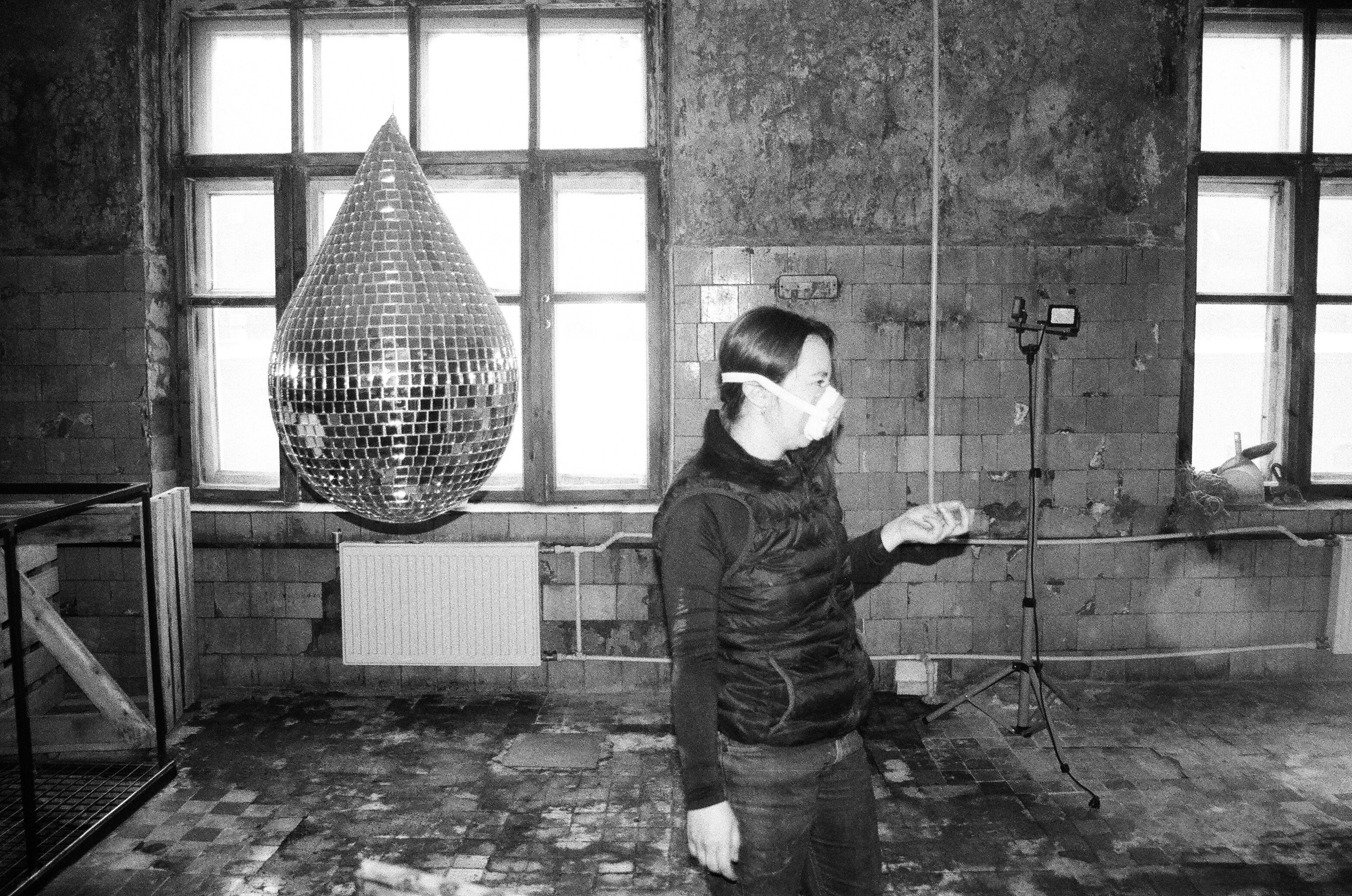 De franc Una dona amb una màscara es troba a l'interior a prop d'una bola de discoteca i parets exposades, creant una atmosfera malhumorada. Foto d'estoc