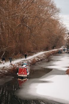 A snowy day along the canal in Newbury, England, with boats and bare trees.