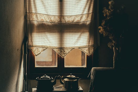 Warm, nostalgic kitchen scene with lace curtains, teapots, and dry flowers on a windowsill.