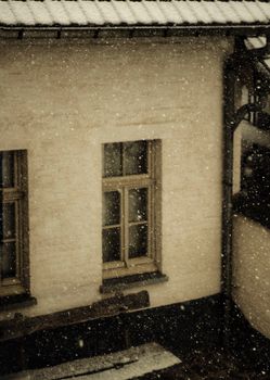 A serene winter scene with snowflakes falling on a rustic building's windows, creating a cozy atmosphere.