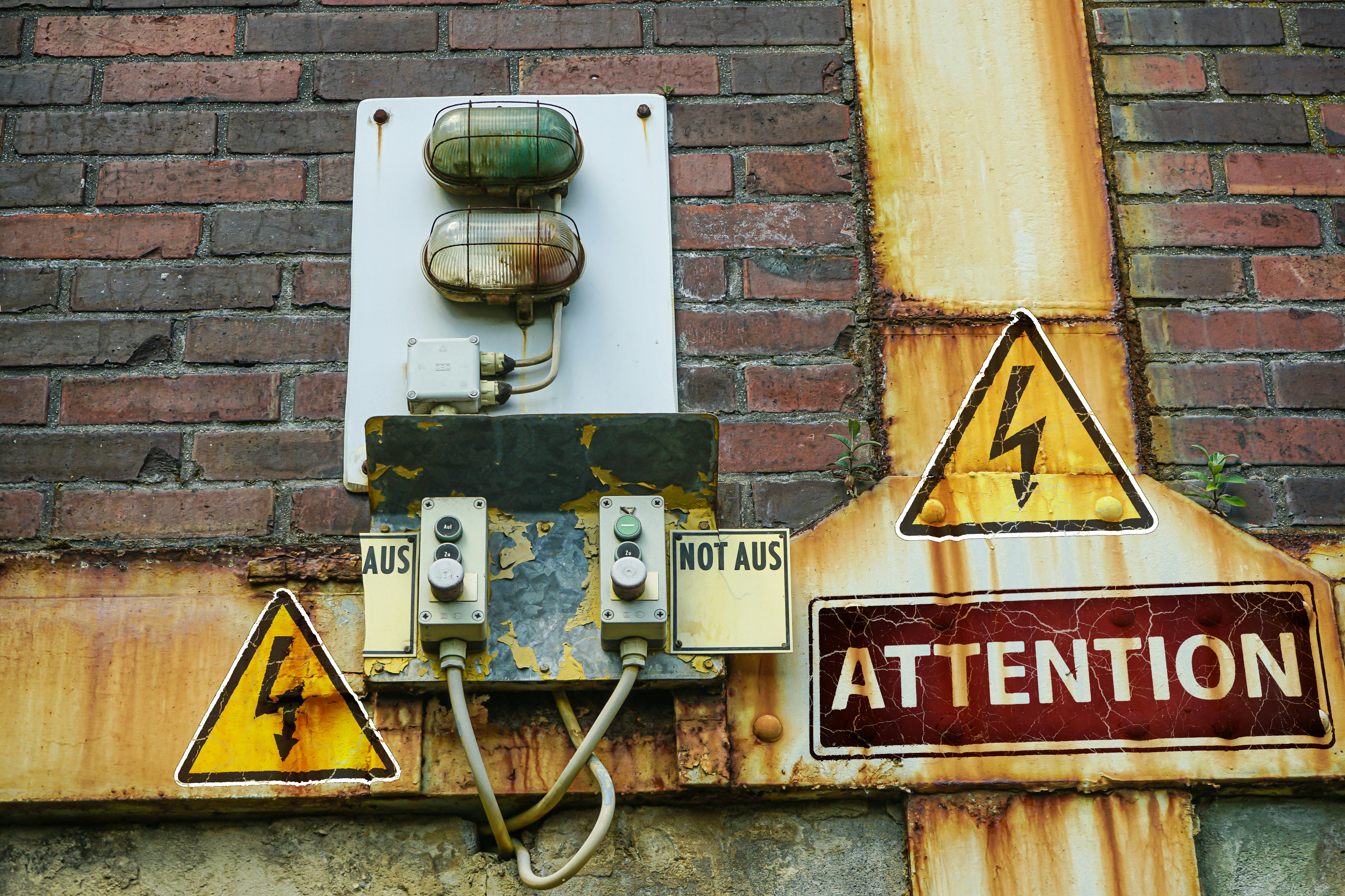 Gratis Et nærbilde av et gammelt, rustent varselskilt og elektriske komponenter på en murvegg som formidler forsiktighet. Arkivbilde