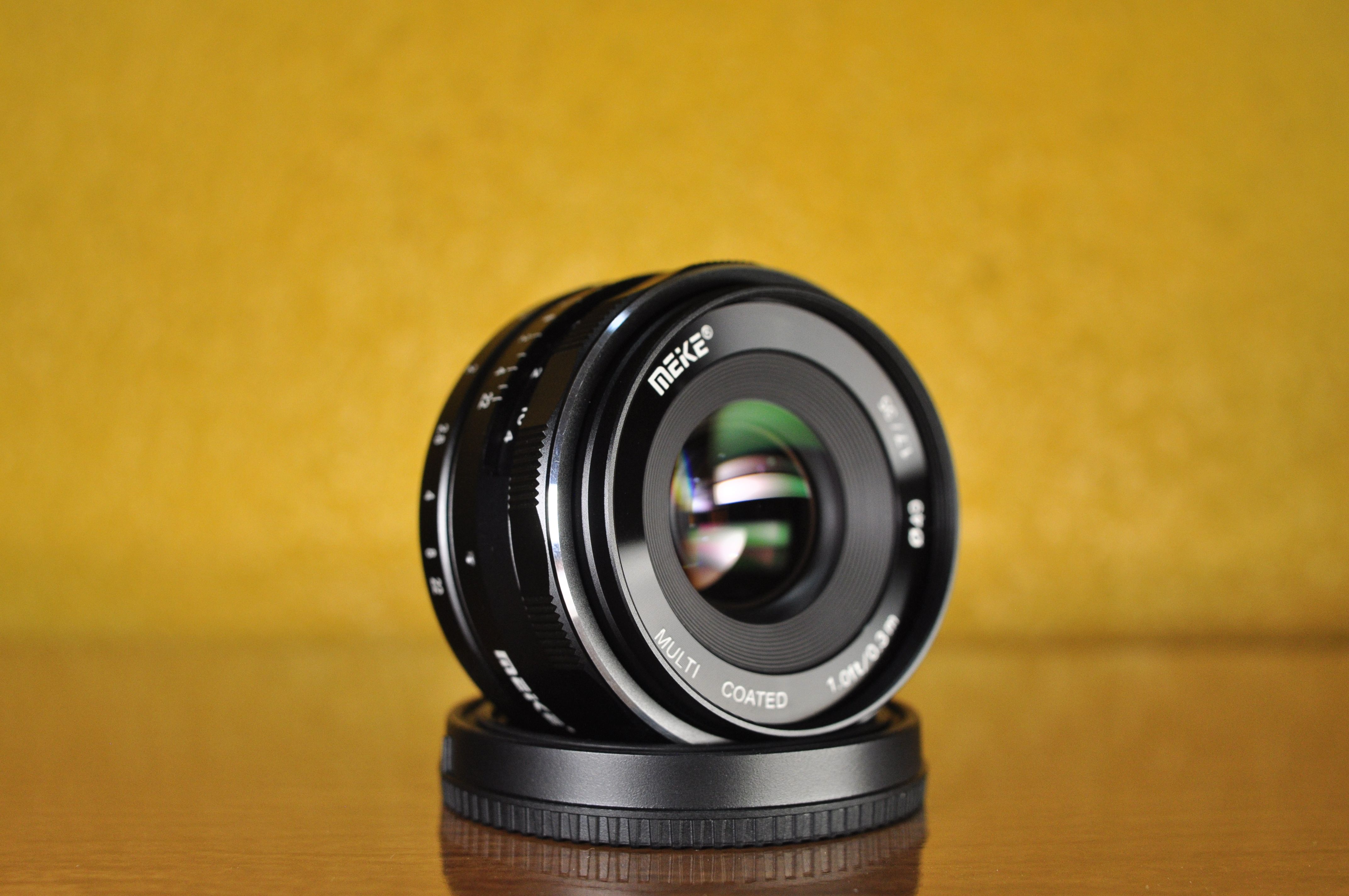 Detailed shot of a Meike lens on a wooden surface with yellow backdrop