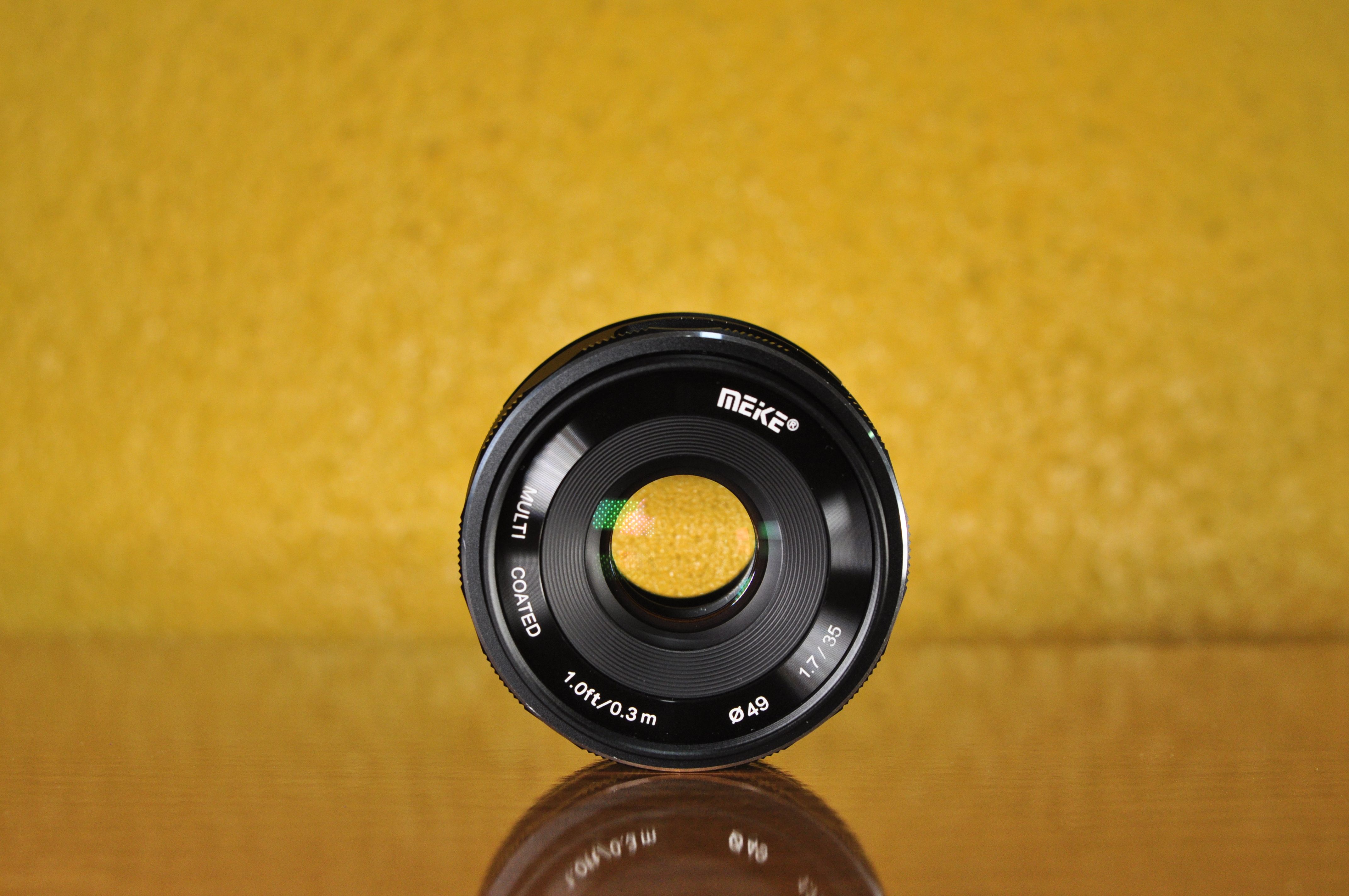 Detailed shot of a Meike camera lens against a vibrant yellow backdrop.