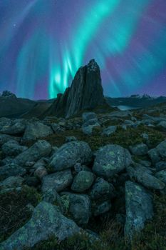 Dramatic aurora borealis illuminating rocky landscape under a starry night sky.
