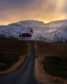 A picturesque church with red roof stands amid a stunning sunset and snow-capped mountains.