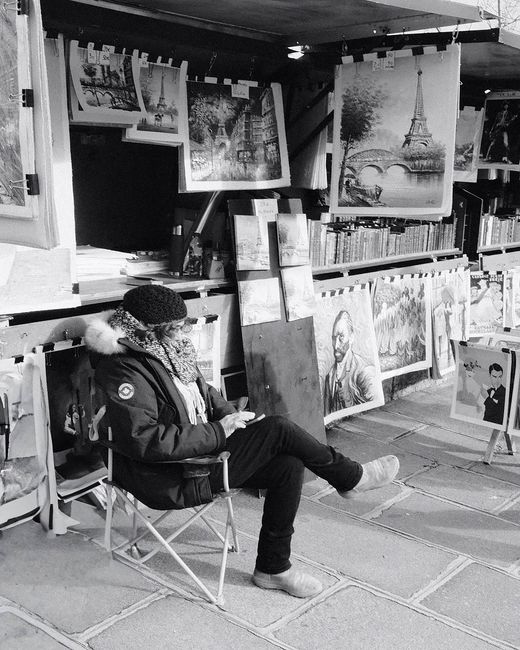 Monochrome photo of a street artist in Paris by the Eiffel Tower displaying artwork.