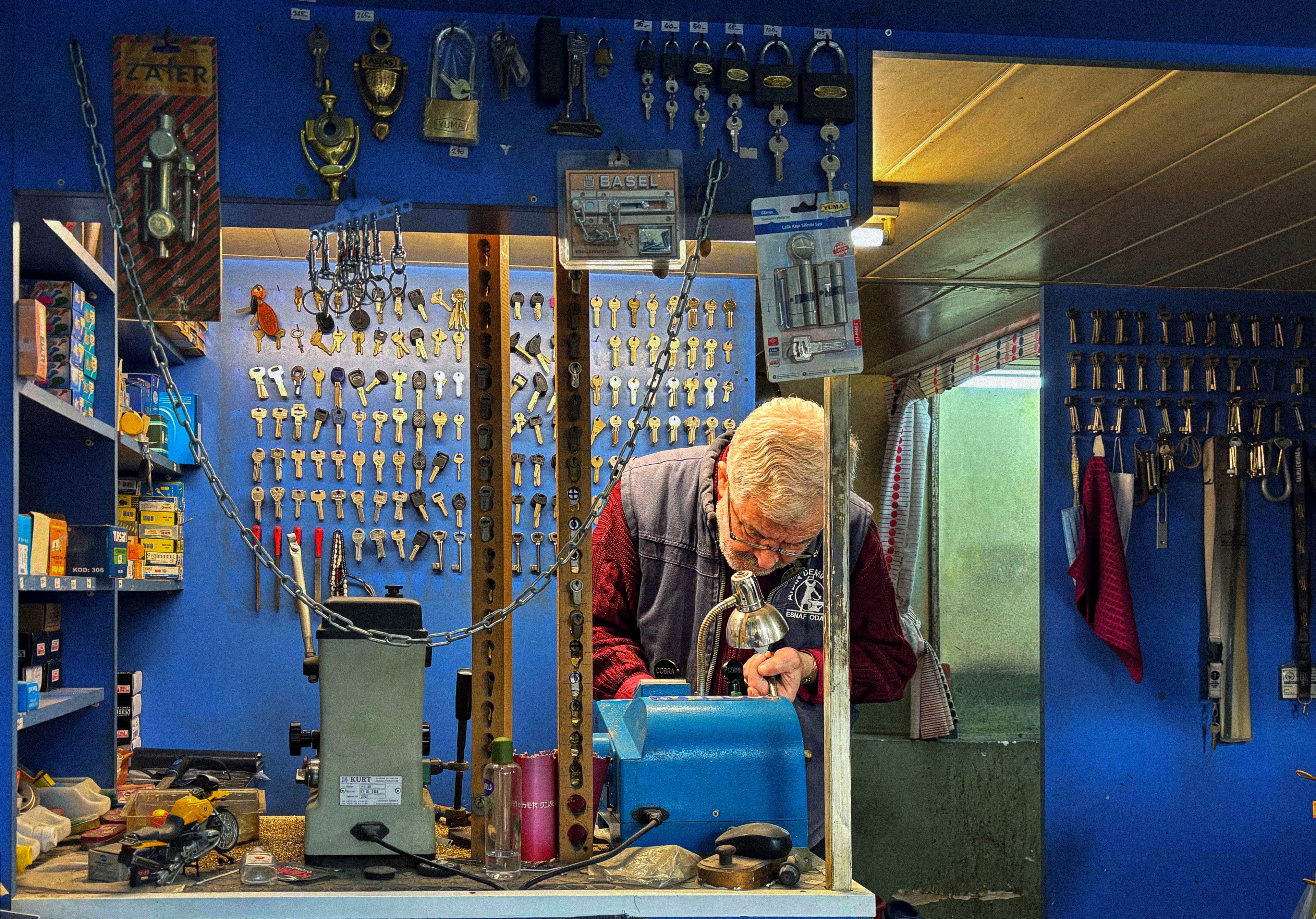 Locksmith at a bench in a key shop lined with hanging key blanks