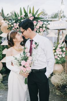 Happy bride and groom embracing with floral background at outdoor wedding.
