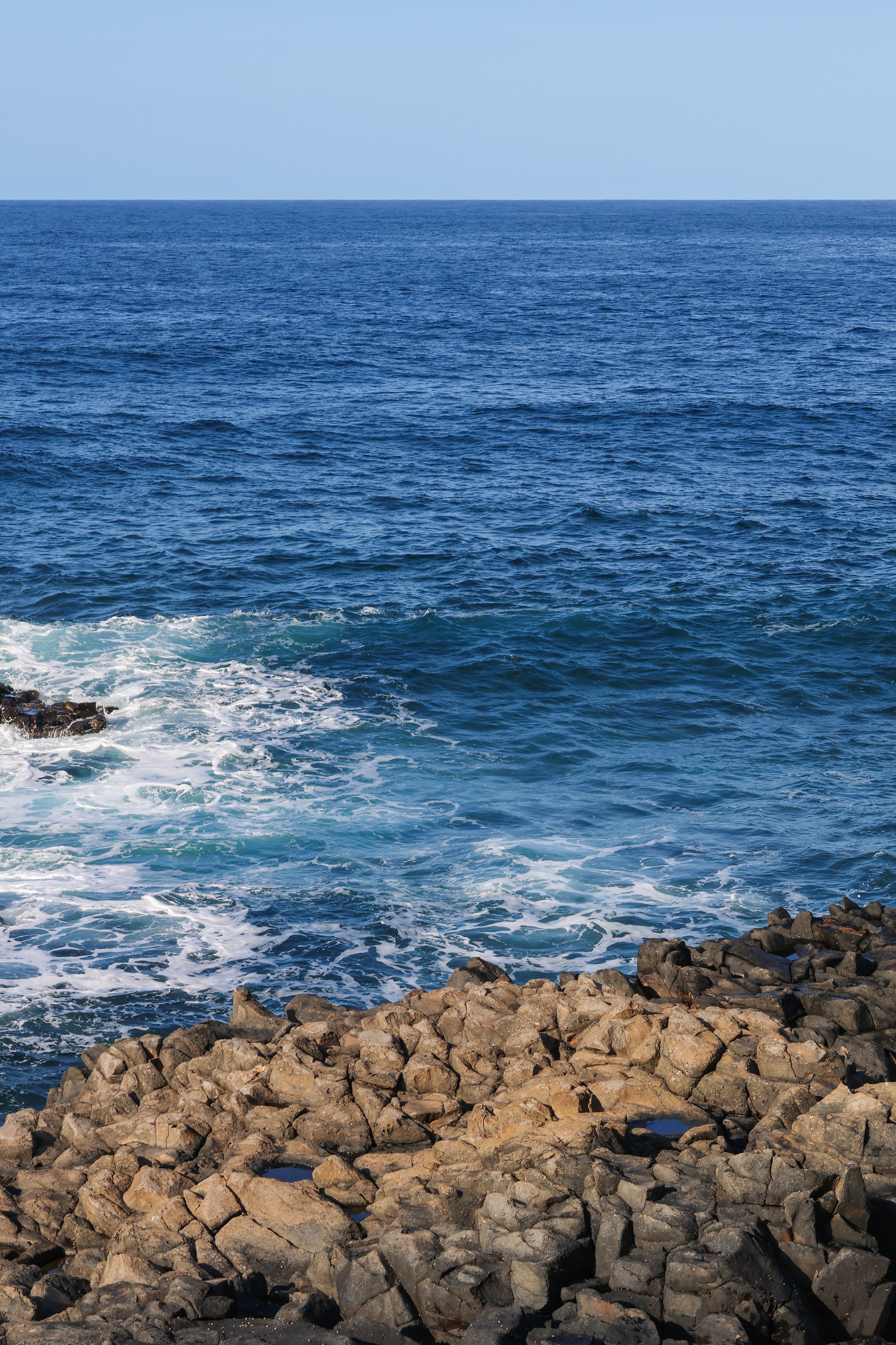 Pristine rocky shoreline with vibrant blue ocean waves at day time.