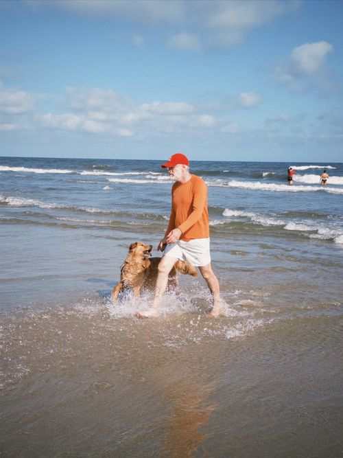 Free Senior man with dog enjoying a beach walk under clear skies. Perfect summer moment. Stock Photo