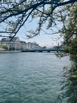 Beautiful riverside view in Zurich with historic buildings and a bridge under a clear sky.