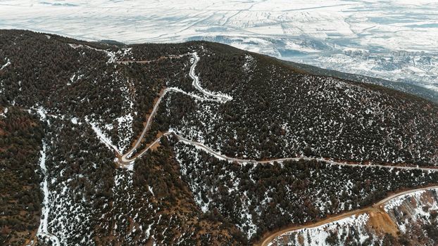 Scenic aerial view of winding road through snow-covered mountains and dense forest.