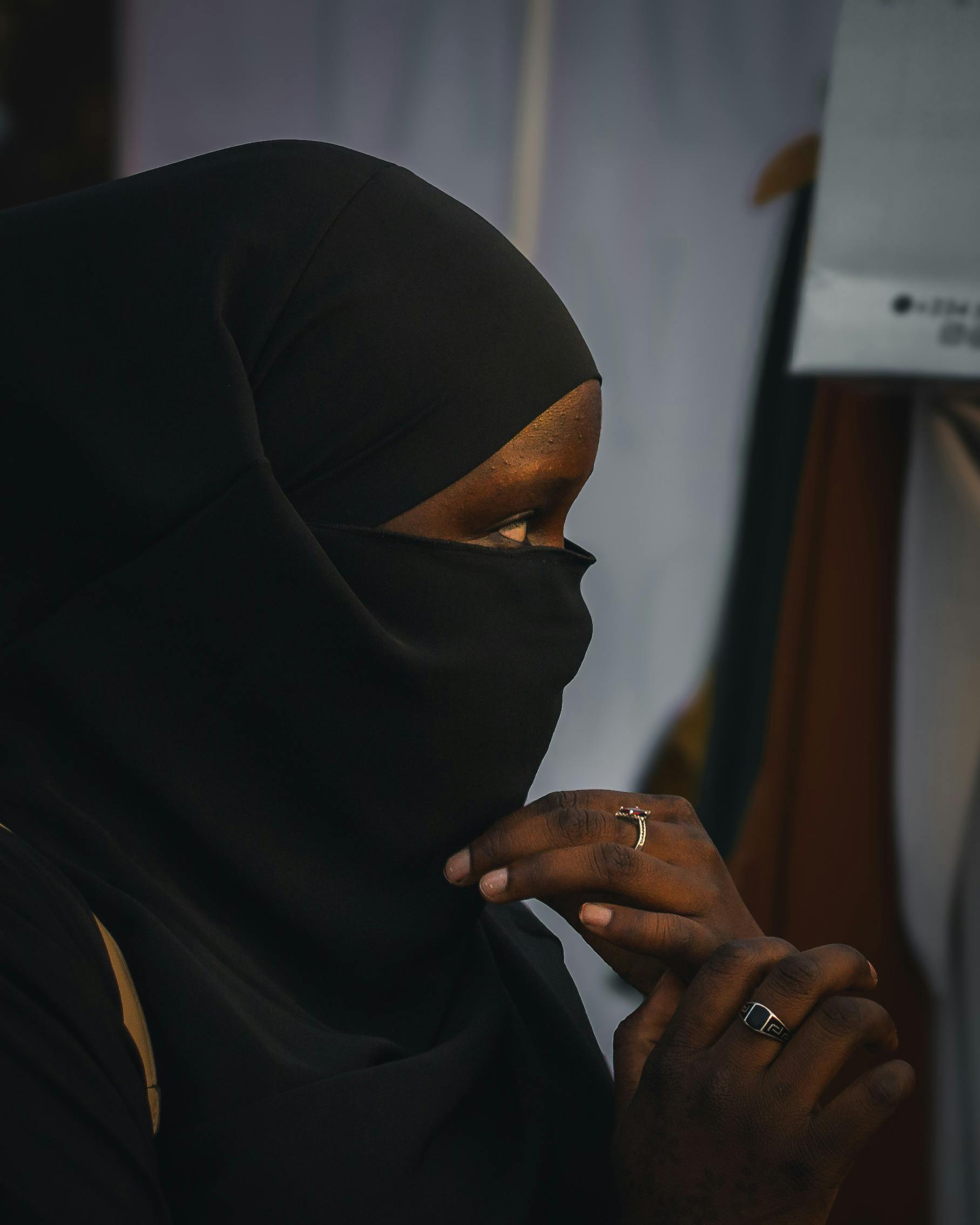 De franc Una dona amb hijab negre, profundament pensativa, amb anells i tapant-se la cara amb les mans. Foto d'estoc