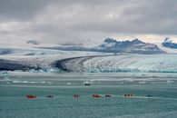 Colorful kayakers paddle near a majestic glacier in Iceland, under a dramatic sky.