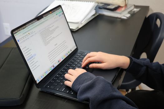 Person typing on a laptop at a desk with papers and books nearby.