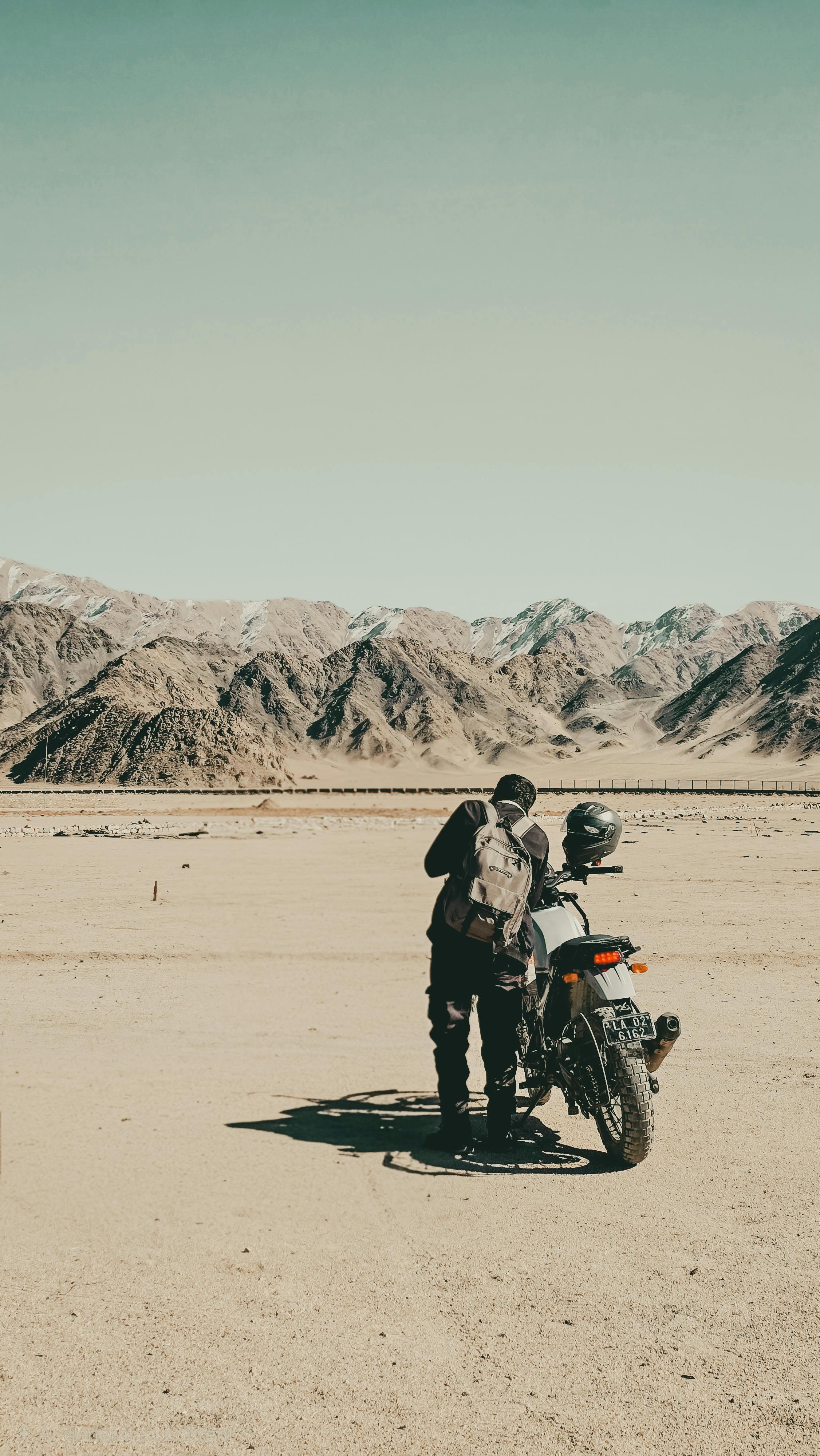 Man with motorcycle in vast desert setting, perfect for adventure seekers.