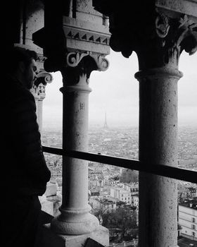 A dramatic black and white view of Paris featuring the Eiffel Tower framed by historic architecture.