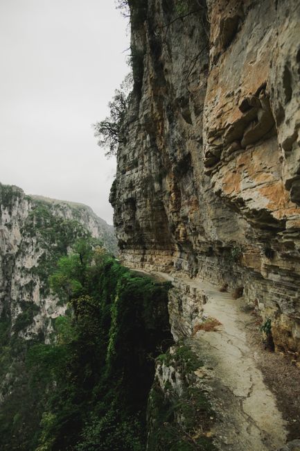 A rugged mountain path clings to a steep cliff, showcasing nature's raw beauty.