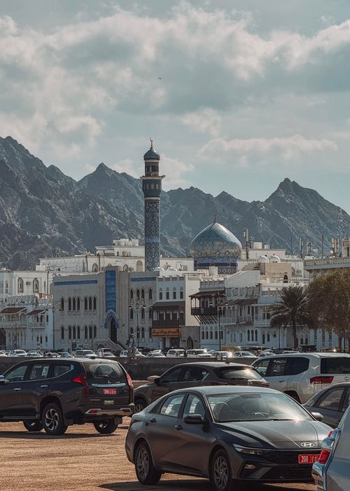 Free Beautiful mosque in Muscat, Oman with mountains and parked cars, showcasing urban landscape. Stock Photo