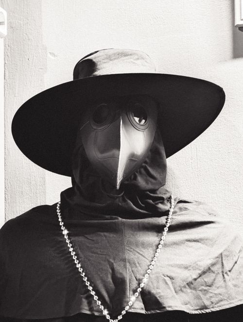 Free Black and white photo of a figure wearing a plague doctor mask and cloak with a wide-brimmed hat. Stock Photo