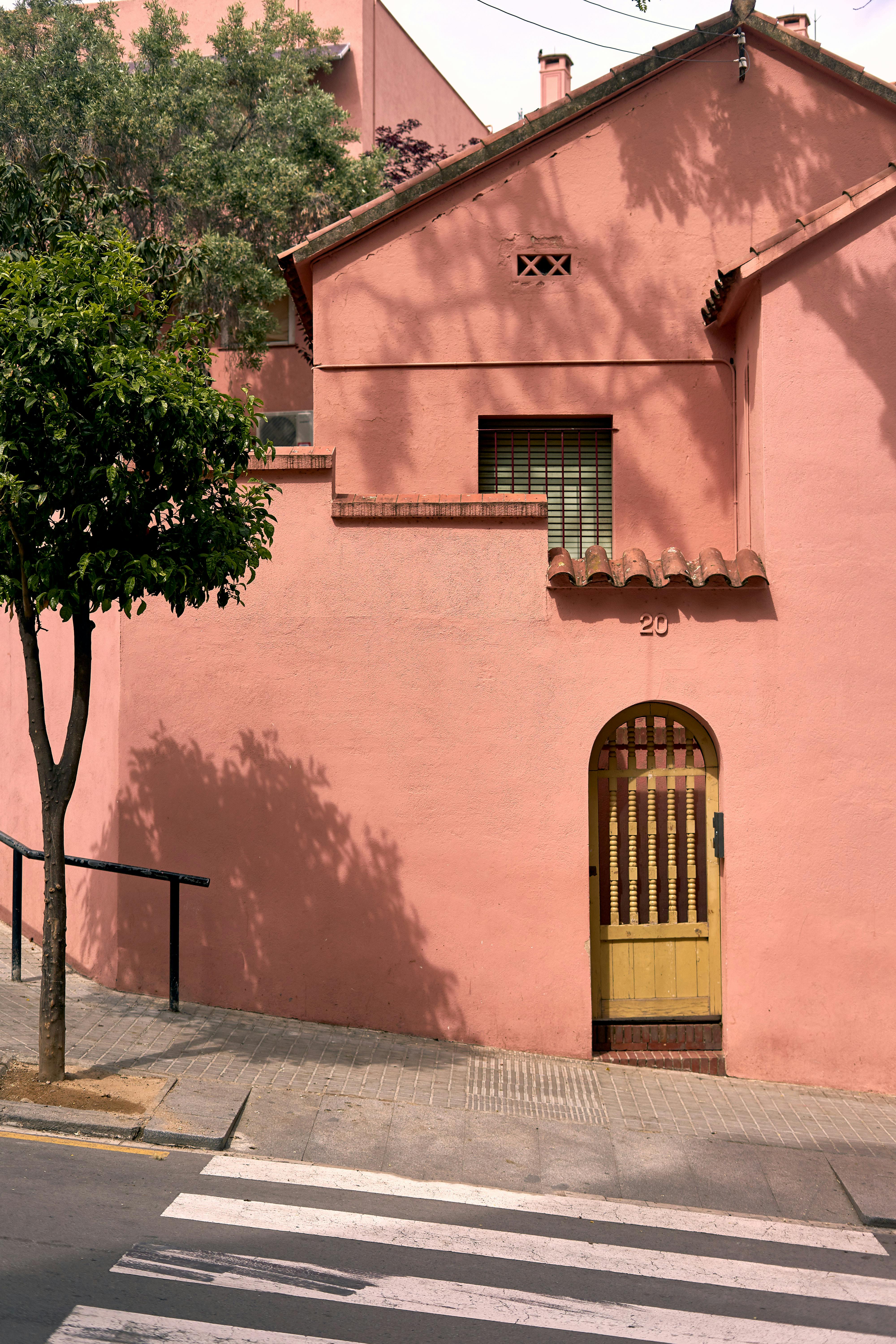 A vibrant pink house with a yellow door in a sunny Barcelona neighborhood.