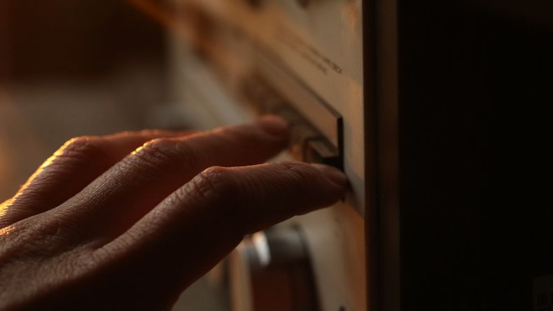 A close-up of a person turning off a light switch next to a doorway as they leave a room