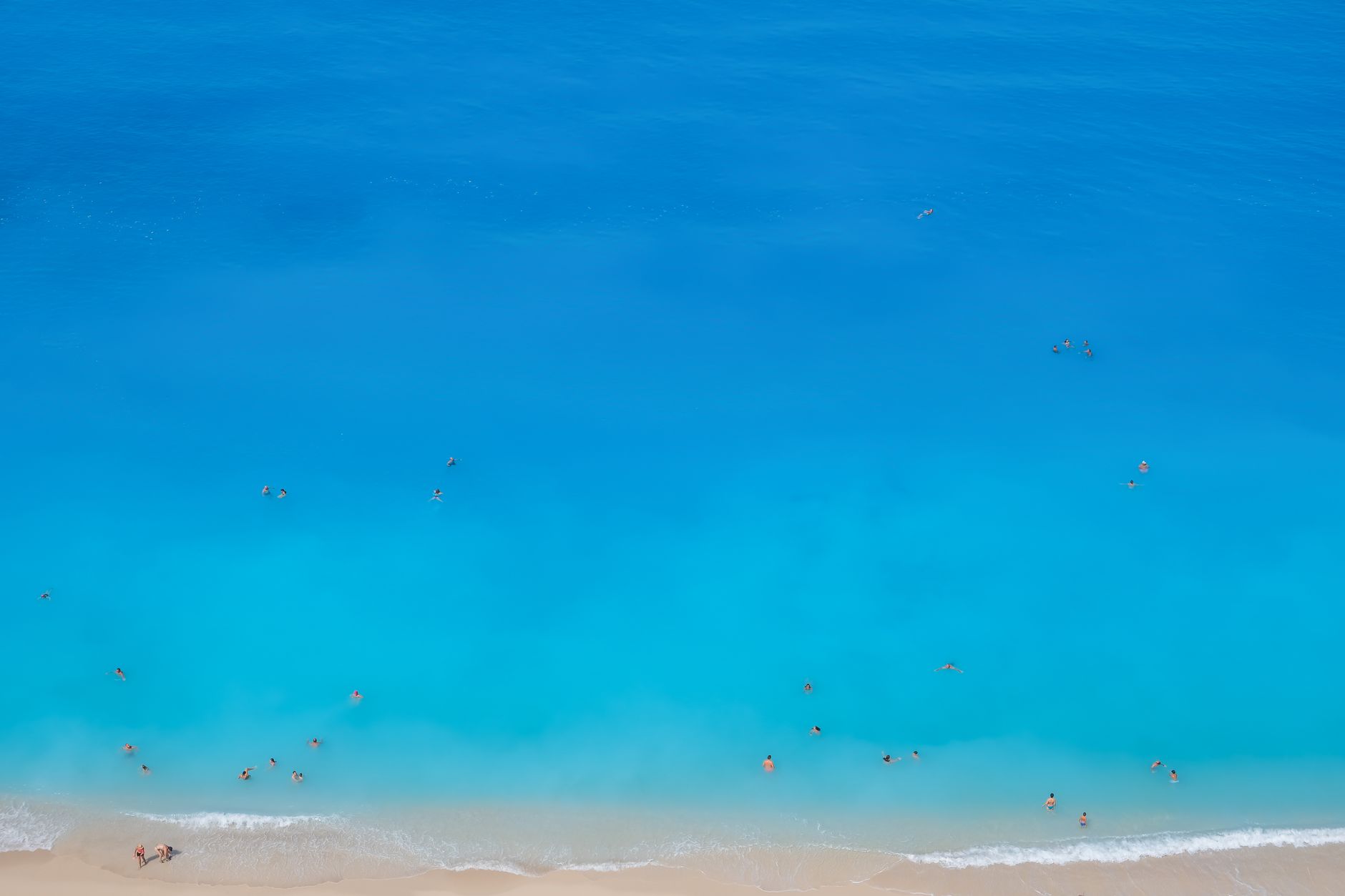 Stunning aerial shot of a Greek beach with turquoise waters and people swimming.
