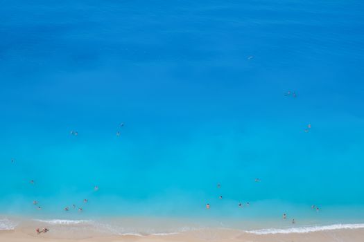Stunning aerial shot of a Greek beach with turquoise waters and people swimming.