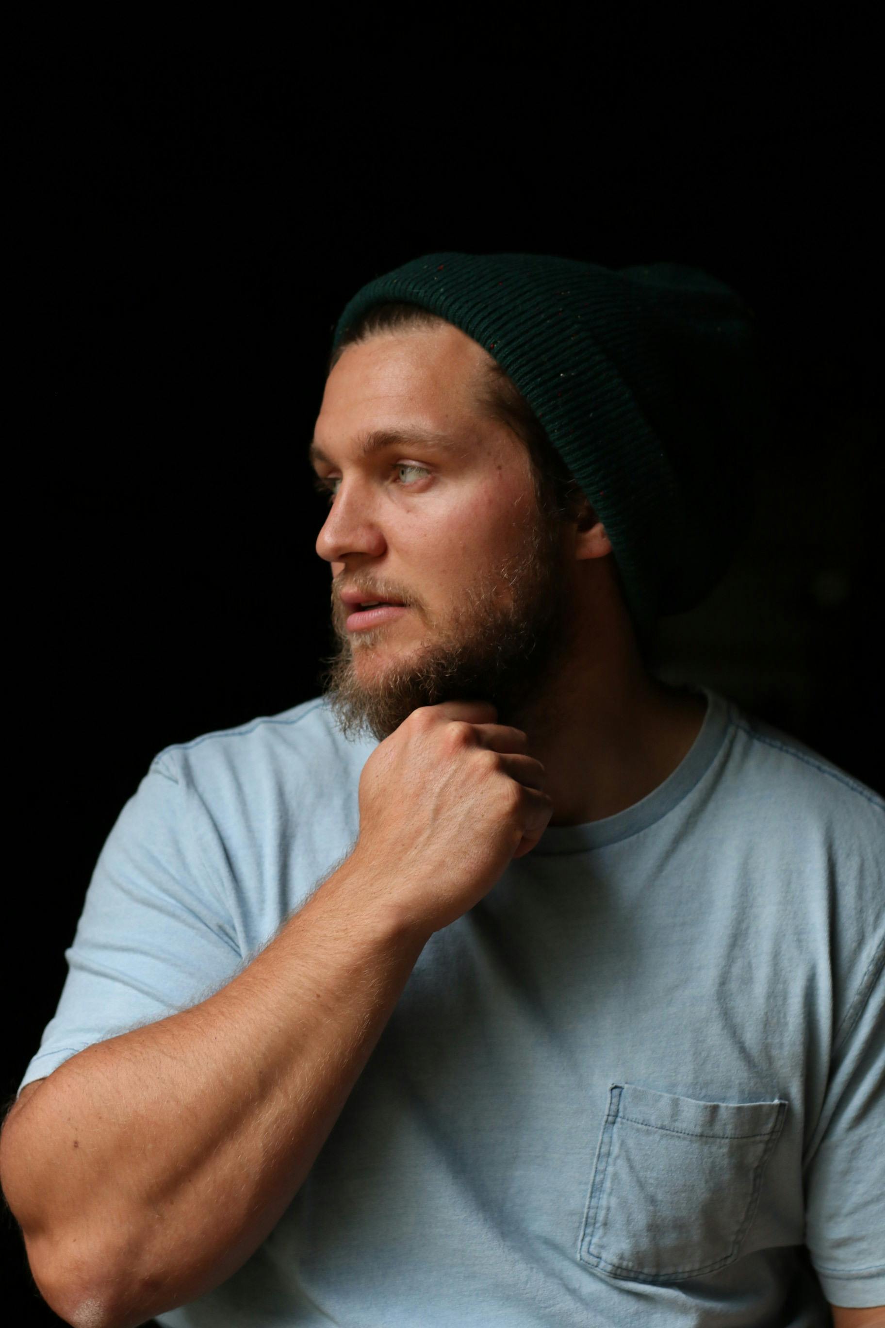A young Caucasian man wearing a beanie, gazing thoughtfully with moody lighting, indoors.