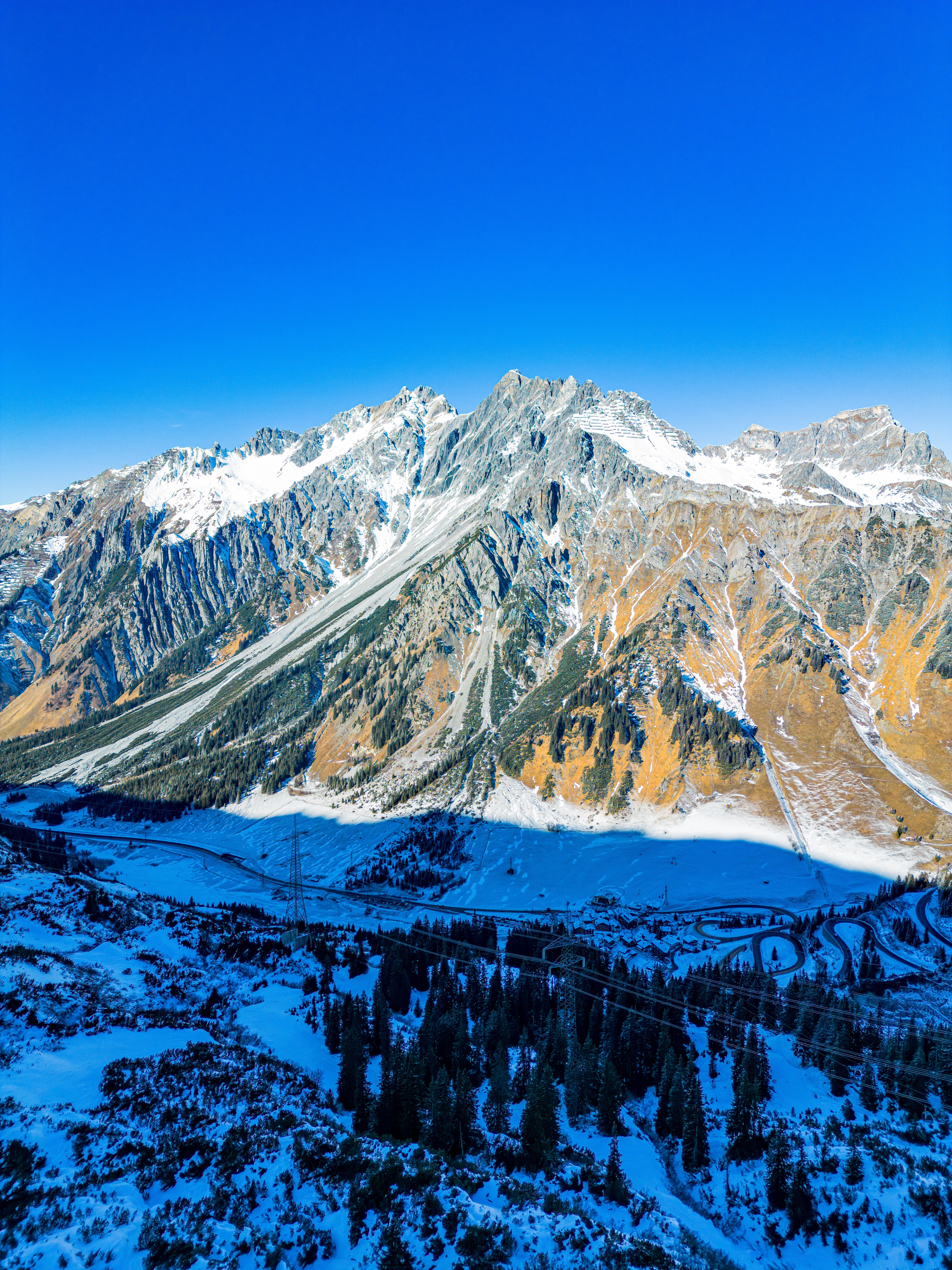A serene aerial view of the Austrian Alps during winter, showcasing rugged snow-capped peaks and a clear blue sky.