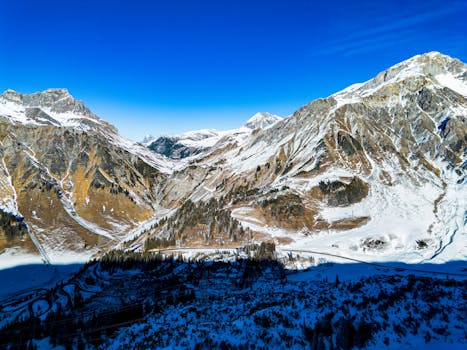 Breathtaking aerial view of snow-covered Austrian Alps with clear blue skies, capturing winter's pristine beauty.