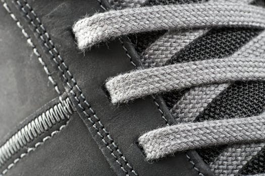 Detailed close-up of a shoe lace intertwined with stitching on a gray sneaker.