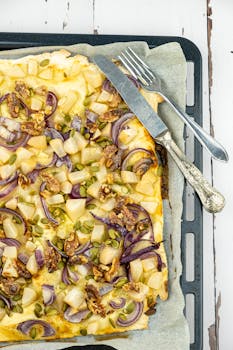 Top-down view of a homemade flammkuchen topped with pears, walnuts, and red onions on parchment paper.