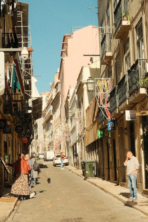 Free Charming sunlit street in Lisbon with people walking and historic architecture. Stock Photo