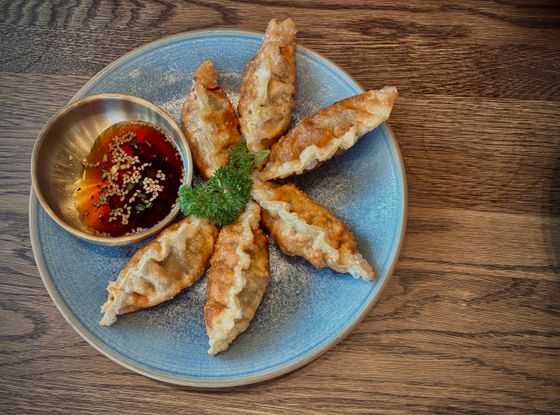 Golden pan-fried gyoza arranged in a star on a blue plate with sesame dipping sauce