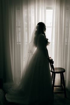 A beautiful bride in silhouette standing beside a window, creating a timeless and romantic scene.