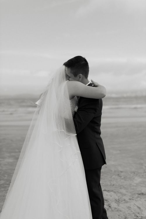 Free A couple embraces on a beach during their wedding, capturing a timeless moment. Stock Photo