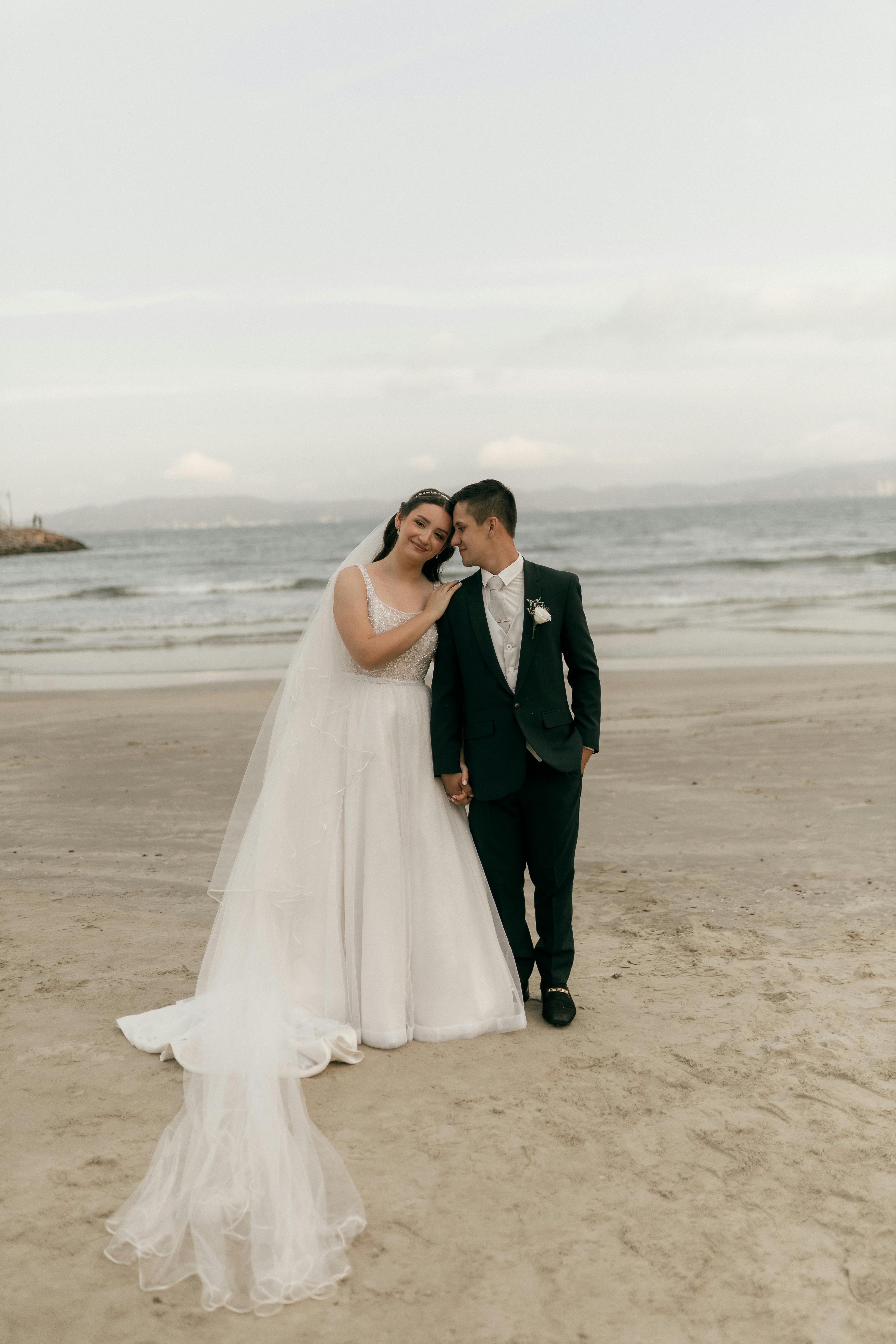 De franc Retrat romàntic d'una parella amb vestit de núvia en una platja serena a la posta de sol, abraçant-se afectuosament. Foto d'estoc