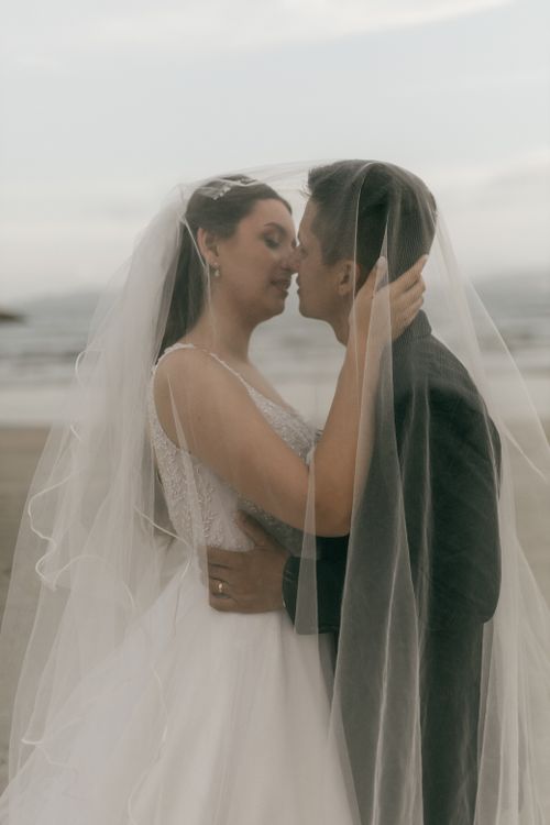 Free Bride and groom intimately embrace under veil on a serene beach, symbolizing love and unity. Stock Photo