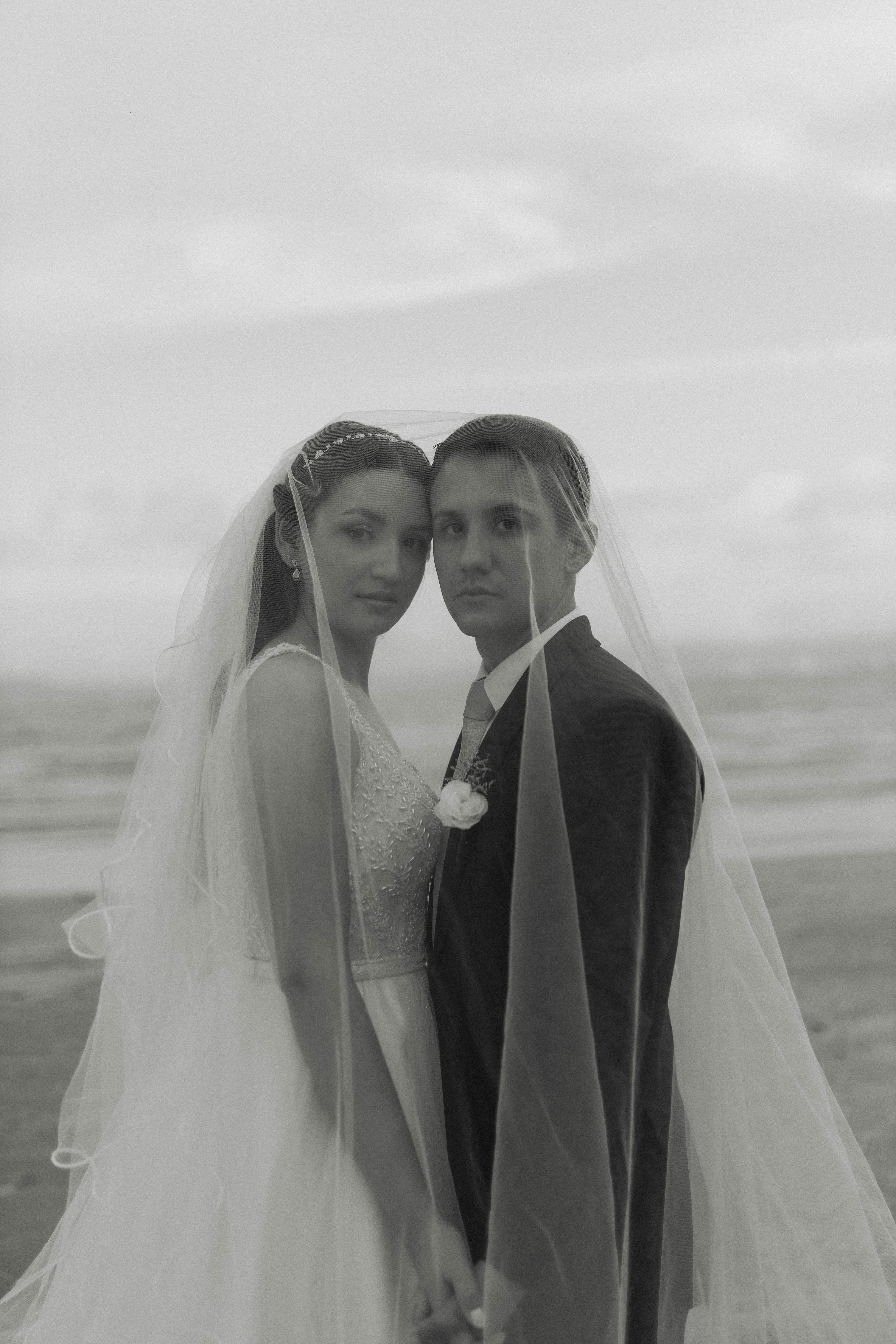 De franc Un retrat atemporal en blanc i negre d'una parella abraçada amb vestit de núvia en una platja serena. Foto d'estoc