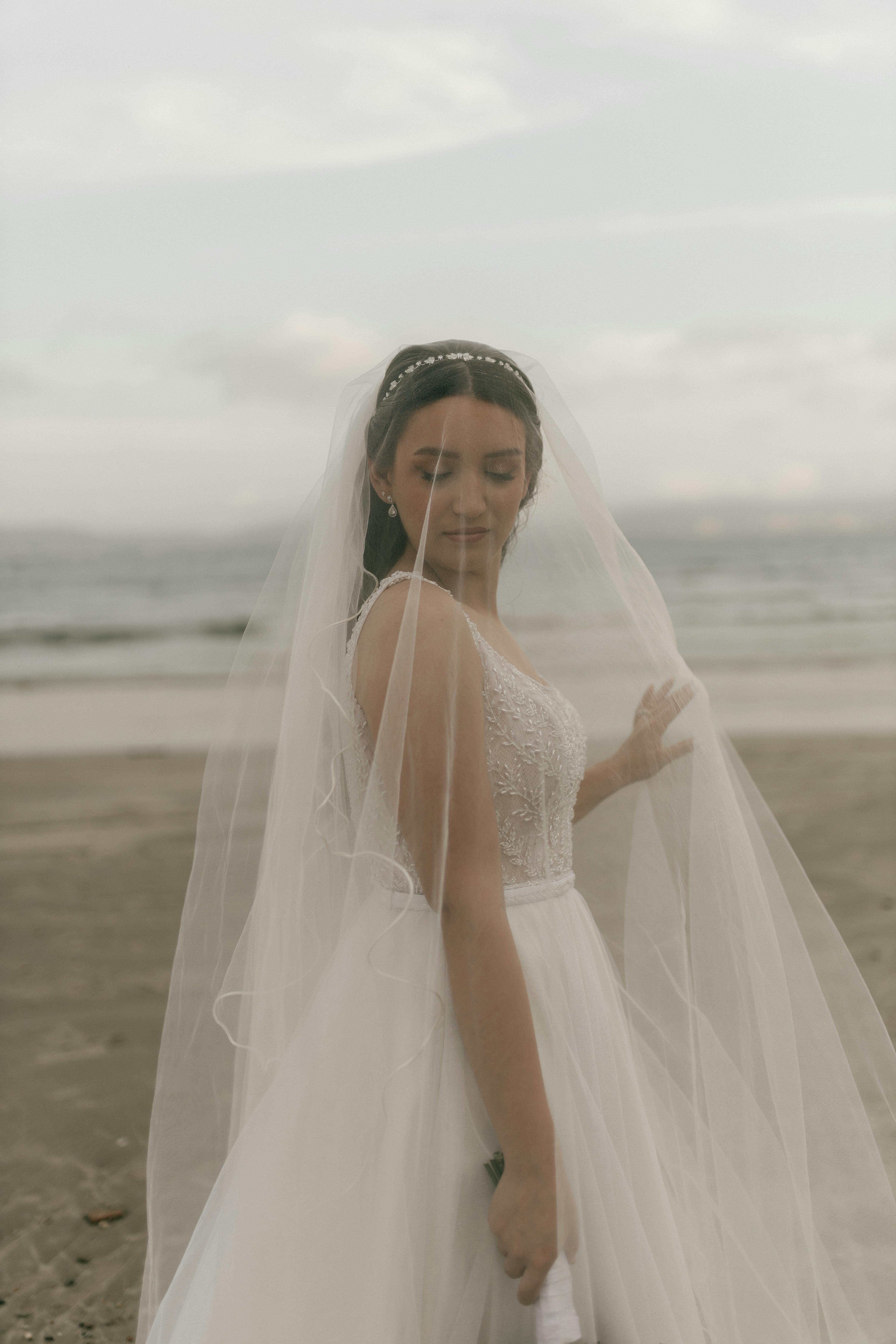 De franc Núvia amb vestit elegant i vel a la platja, un entorn suau i natural. Foto d'estoc