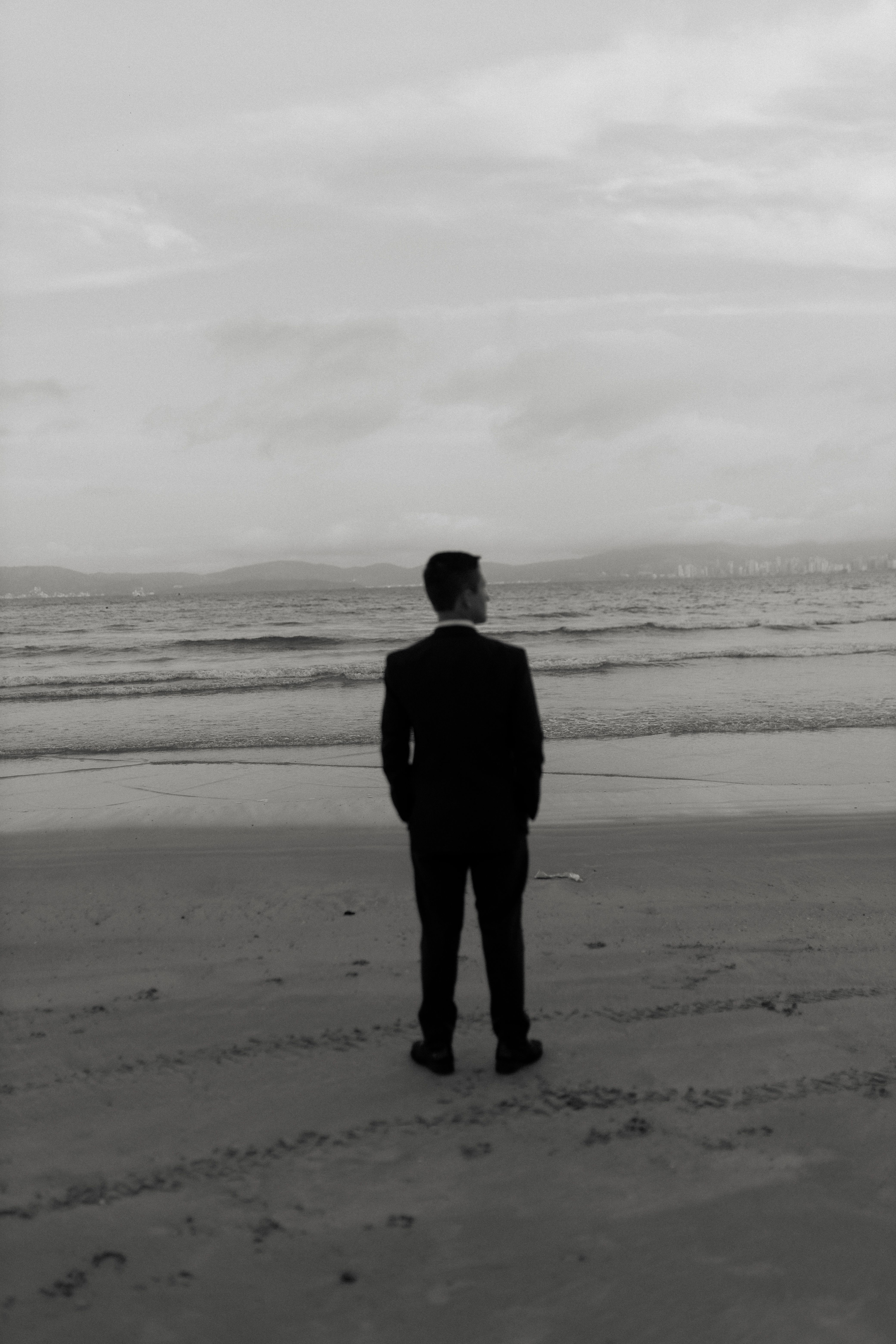 A man standing alone on a quiet beach in contemplation — the integration period after ibogaine ceremony for PTSD is when the neuroplasticity window is used productively or wasted