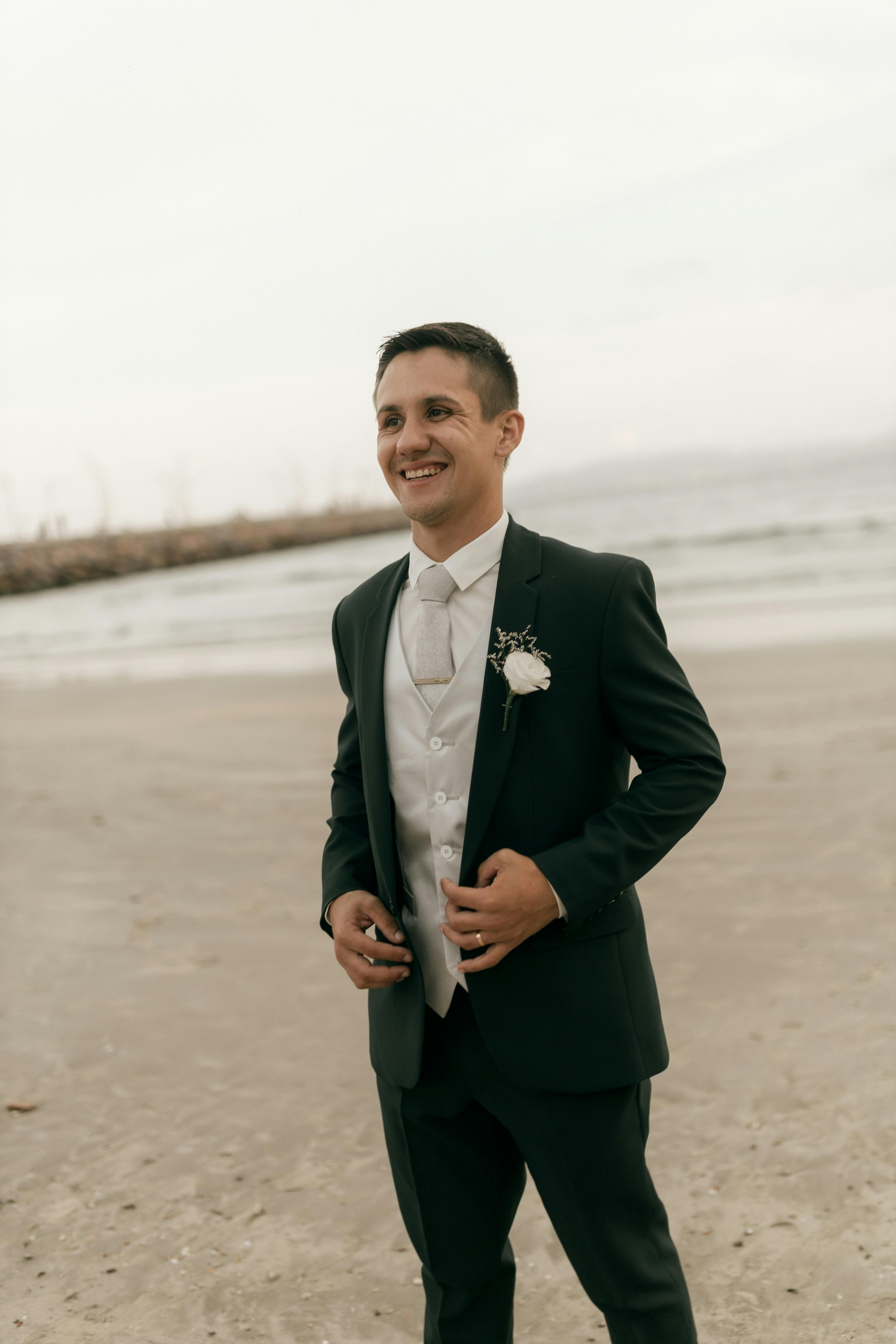 De franc Un nuvi amb vestit formal somrient en una platja de sorra durant una cerimònia de casament. Foto d'estoc