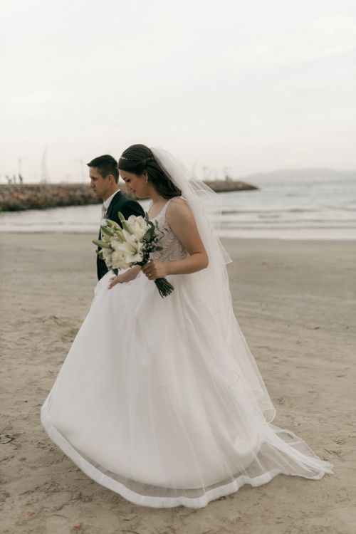 Free Bride and groom walking on the beach during a serene wedding ceremony. Stock Photo