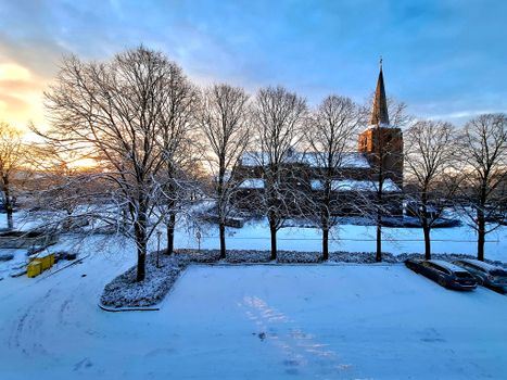 Winter scene with a church and snow-covered trees at sunset.