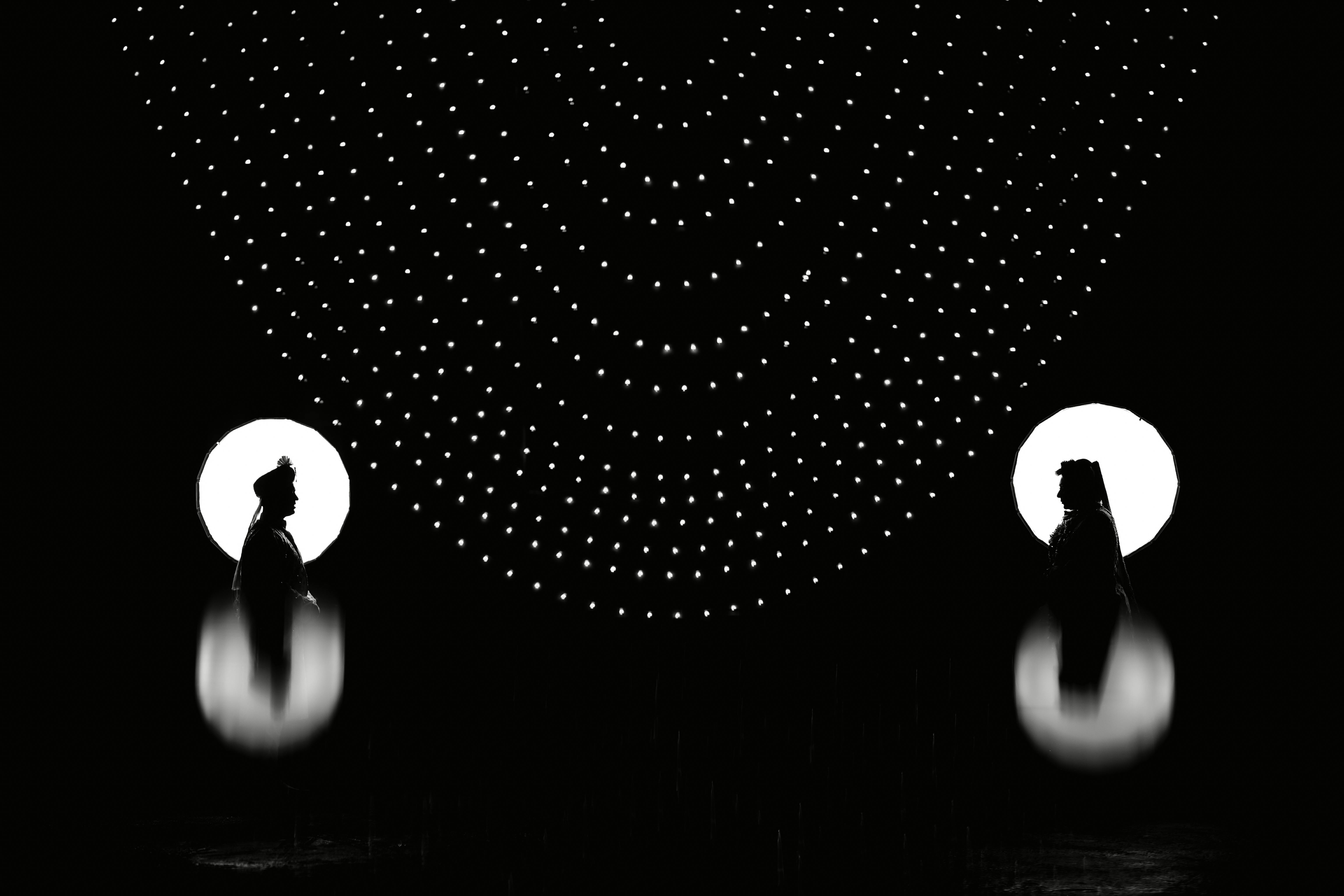 grátis Silhueta artística em preto e branco de duas figuras sob um padrão de luzes. Foto profissional