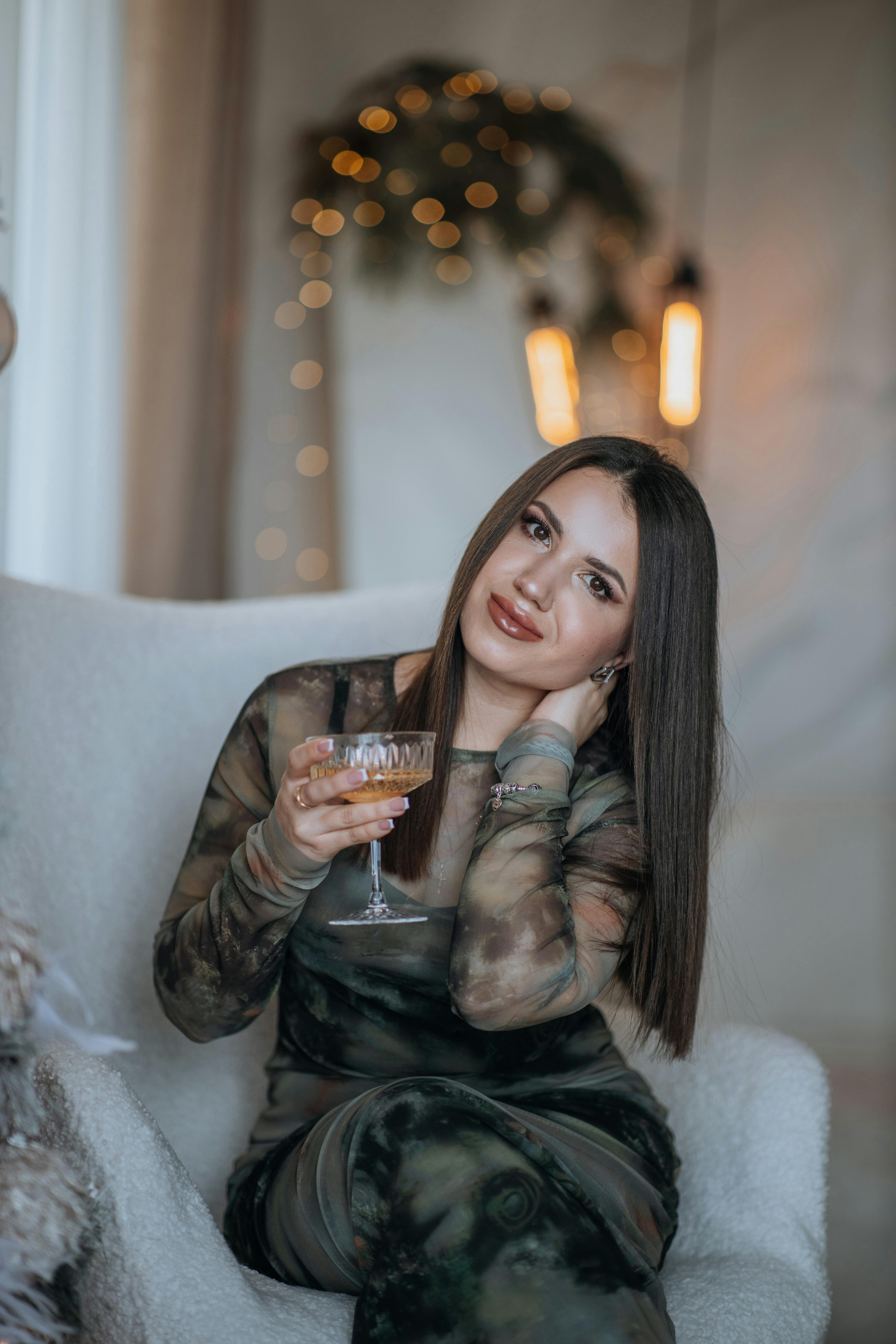 De franc Una dona elegant amb els cabells llargs gaudint d'una copa de vi en una butaca còmoda amb una il·luminació suau. Foto d'estoc