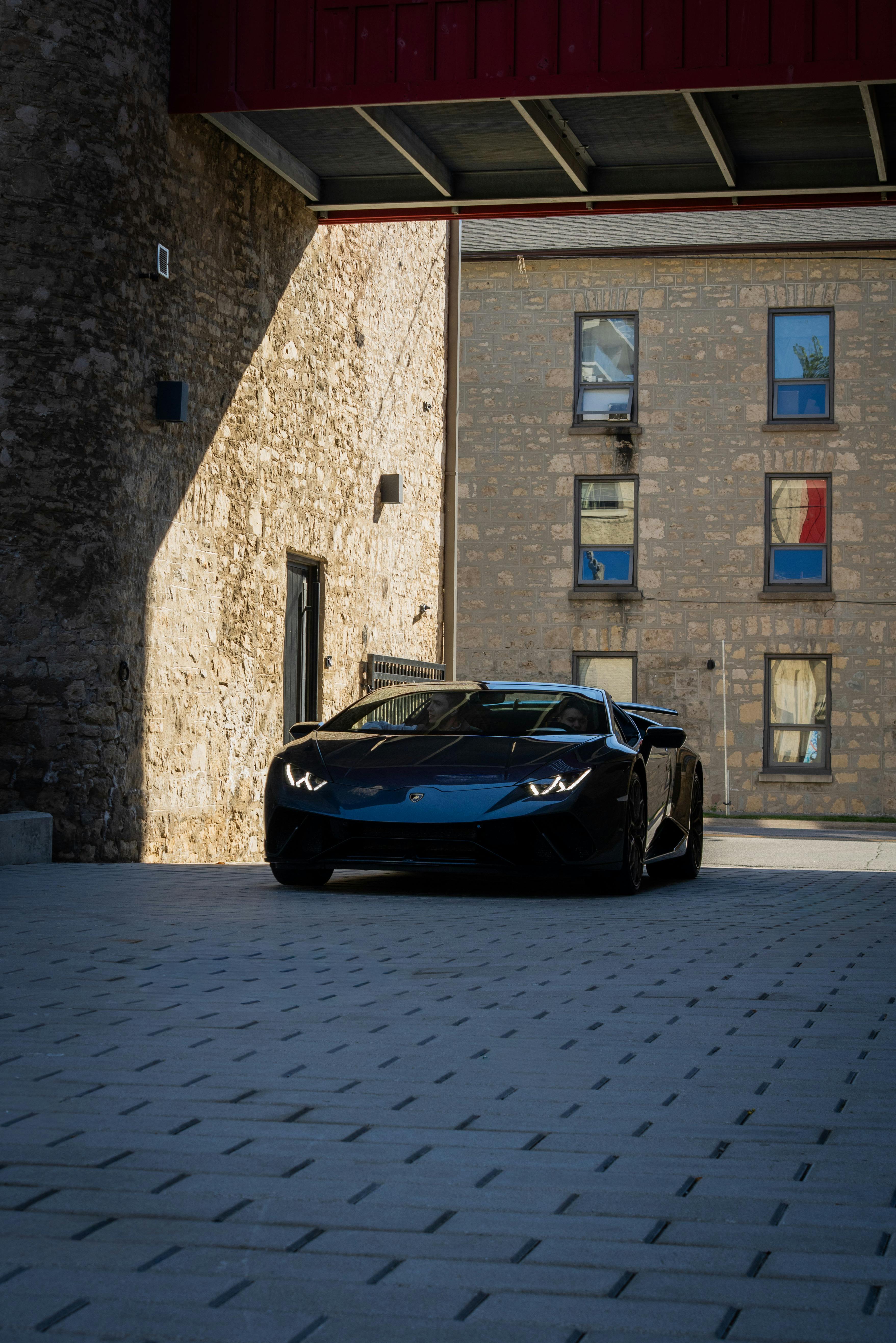 De franc Un cotxe esportiu negre modern aparcat en un carreró urbà ombrívol amb edificis de pedra. Foto d'estoc