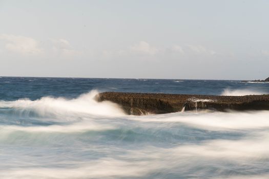 Calm ocean waves softly crashing against a rocky shoreline, capturing the essence of coastal tranquility.
