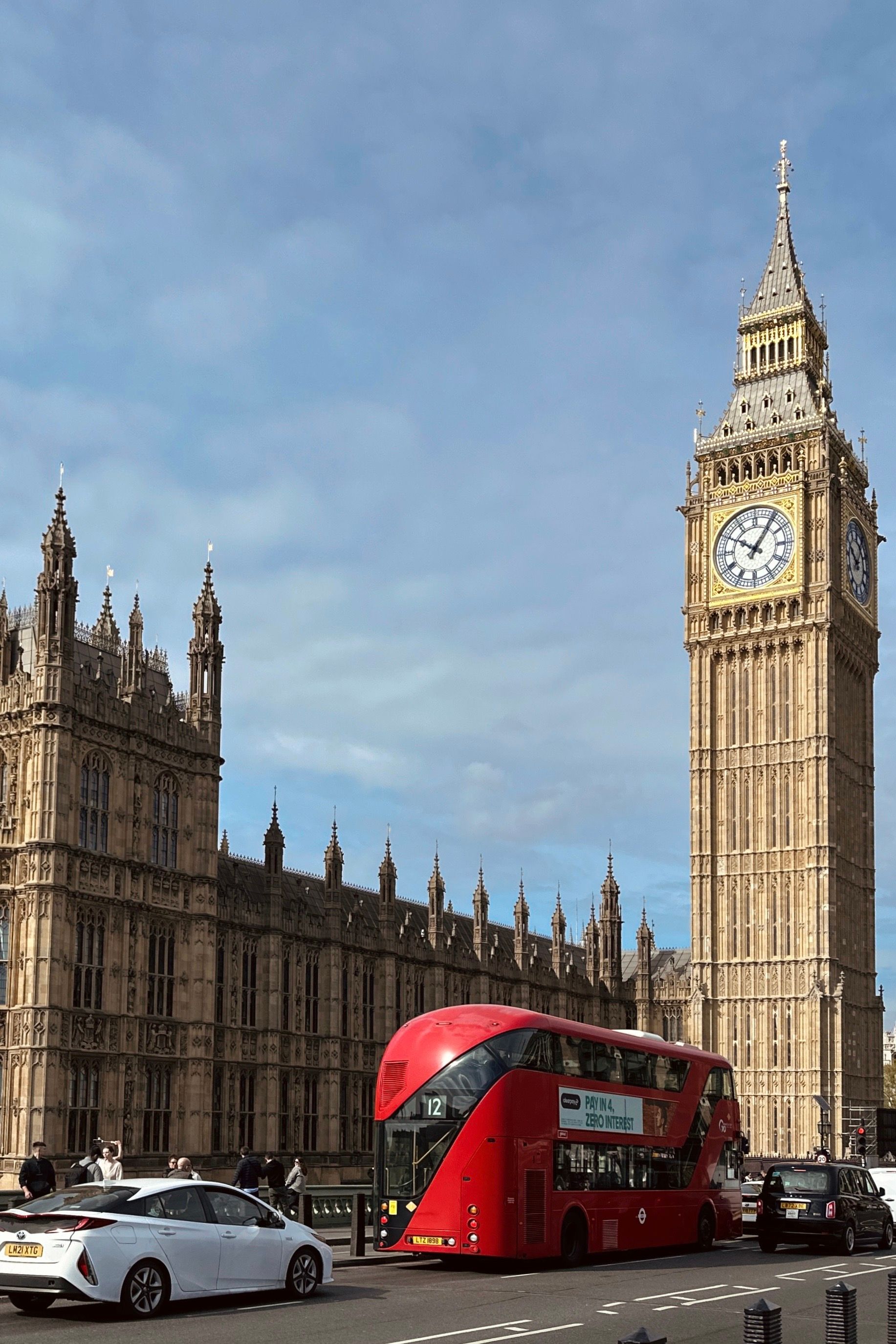 Red open-top hop-on hop-off London sightseeing bus passing the Houses of Parliament and Big Ben on a clear day